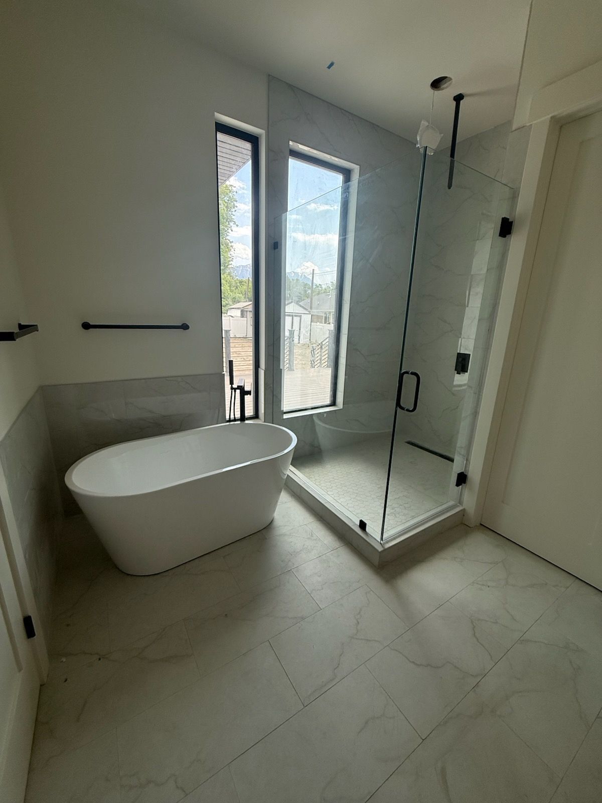 Modern bathroom with a white freestanding tub, glass shower, and large window.