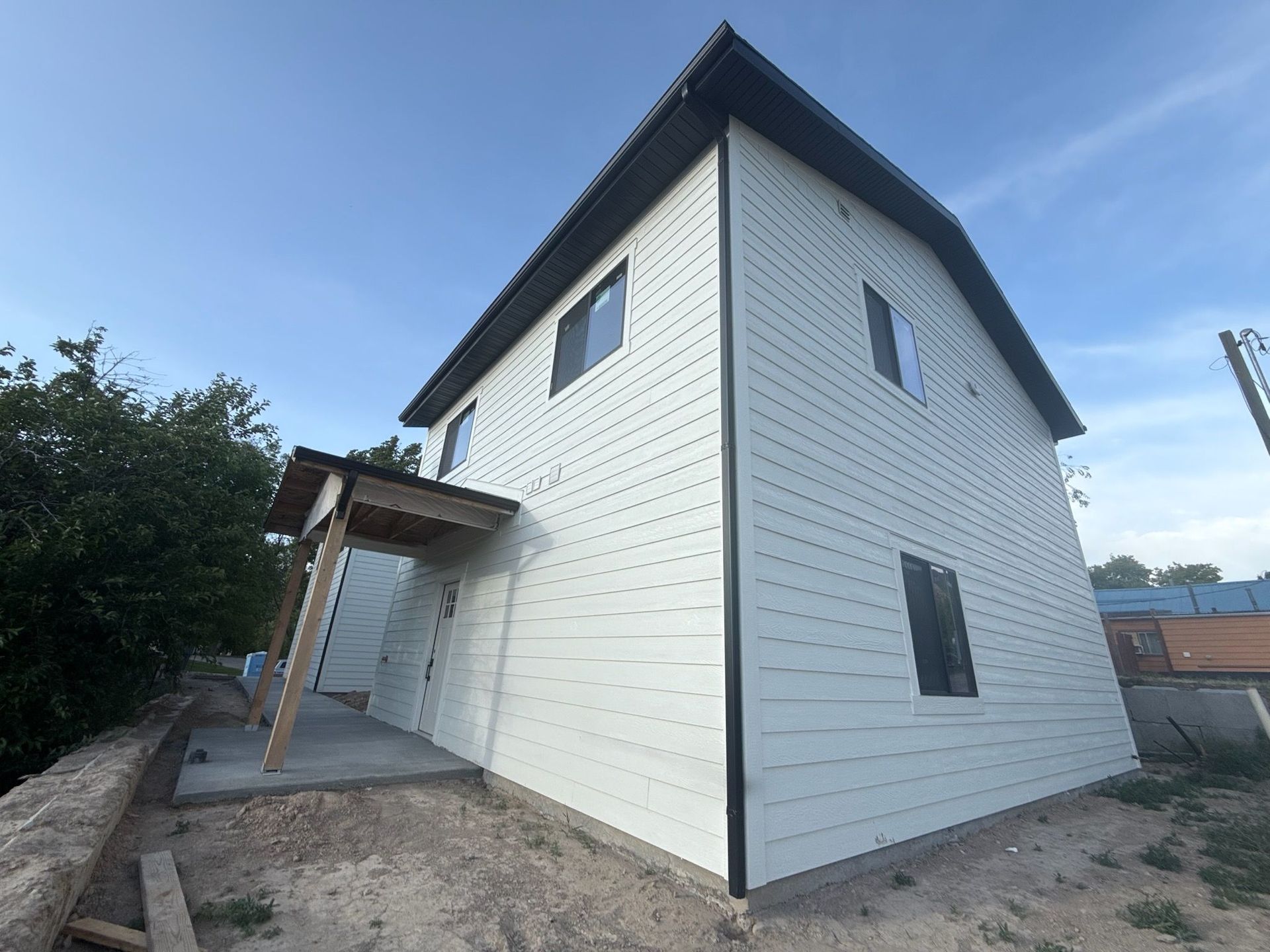 Two-story house with light siding, dark trim, and a small porch. Exterior shot with blue sky.