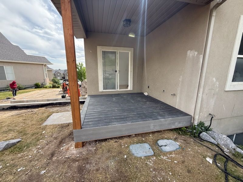 Deck with gray boards, next to house with sliding door. Brown support beam. Grass and gravel foreground.