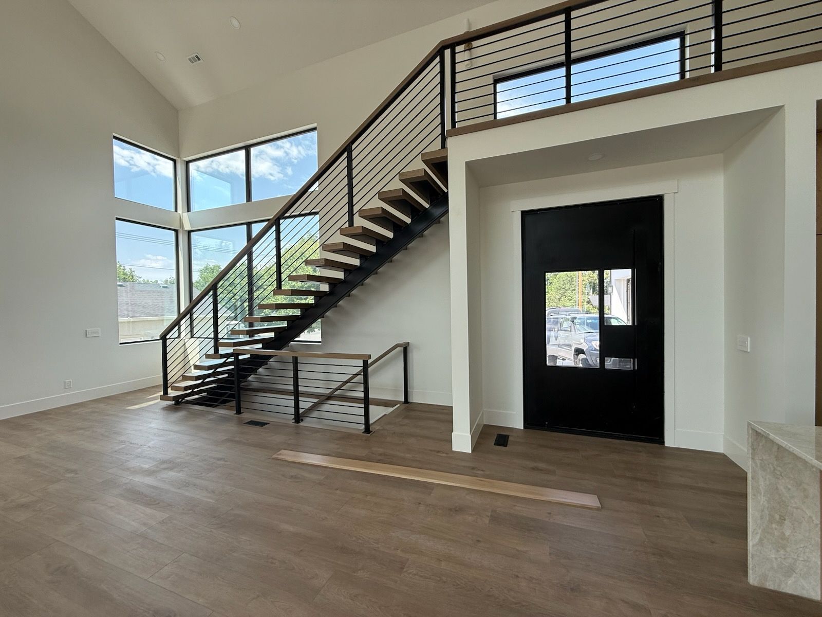 Interior with stairs and black door. Large windows, wood floors, and black railing.