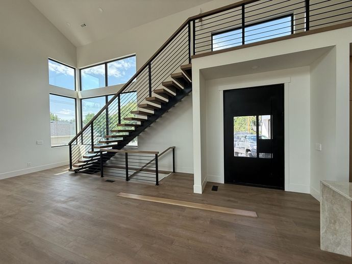 Interior with stairs and black door. Large windows, wood floors, and black railing.