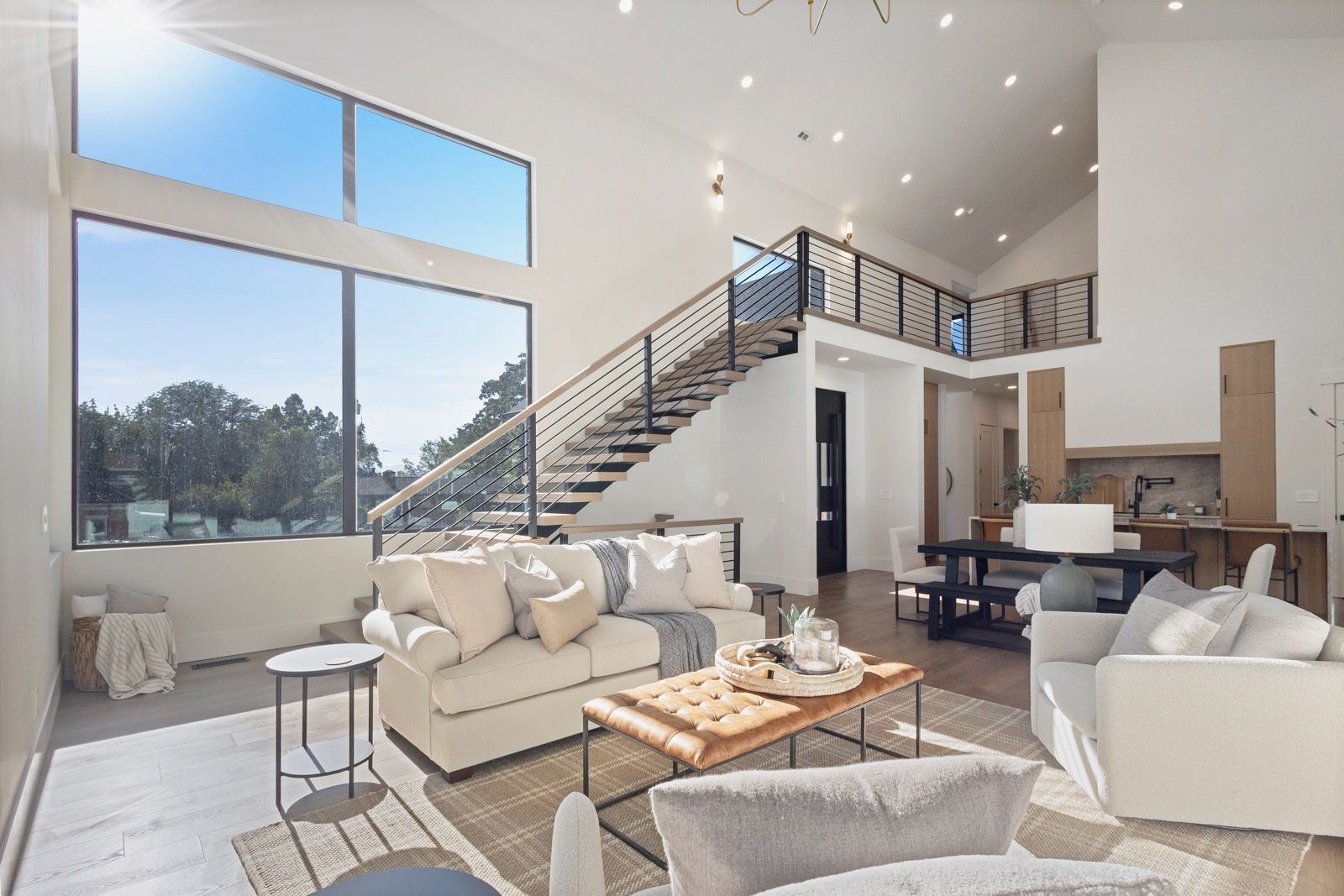 Spacious living room with high ceilings, large windows, staircase, and white sofas.