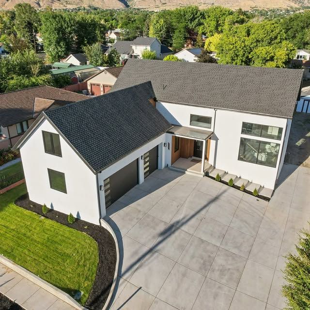 Modern two-story white house with black roof and garage. Concrete driveway, green lawn.