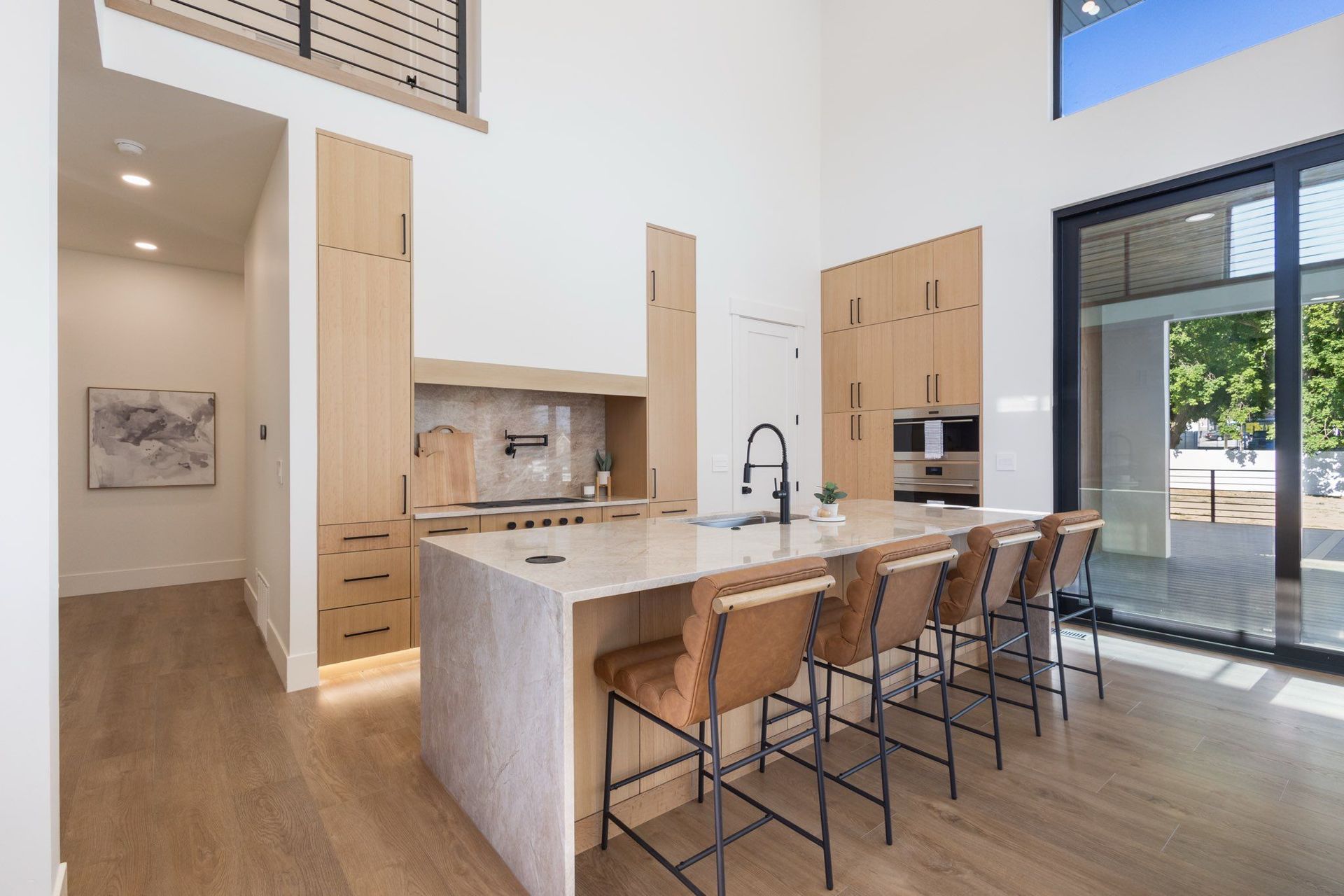 Modern kitchen with light wood cabinets, large island with stools, and sliding glass door.
