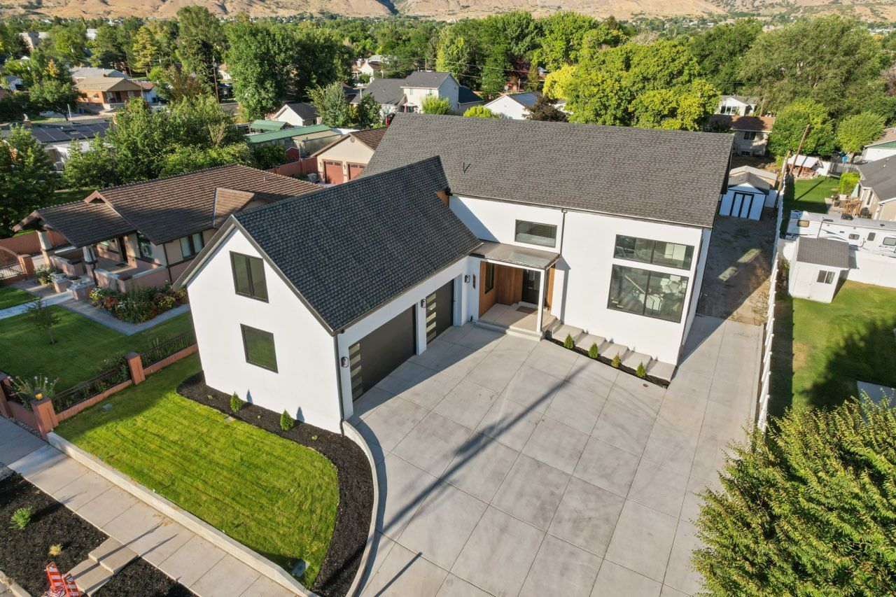 Modern white house with dark gray roof and garage, concrete driveway, and green lawn.