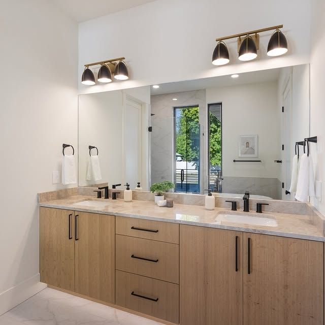 Bathroom with a large mirror over a light wood vanity, black fixtures, and sconces.