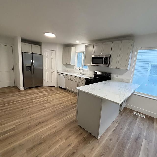 Modern kitchen with gray cabinets, stainless steel appliances, and wood floors.