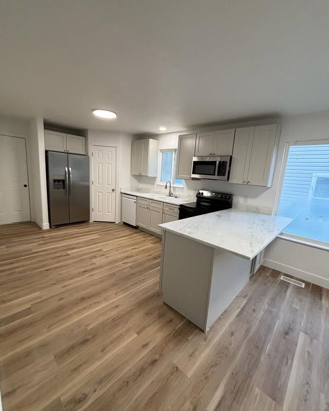 Modern kitchen with light wood floors, white cabinets, stainless steel appliances, and an island with a white countertop.