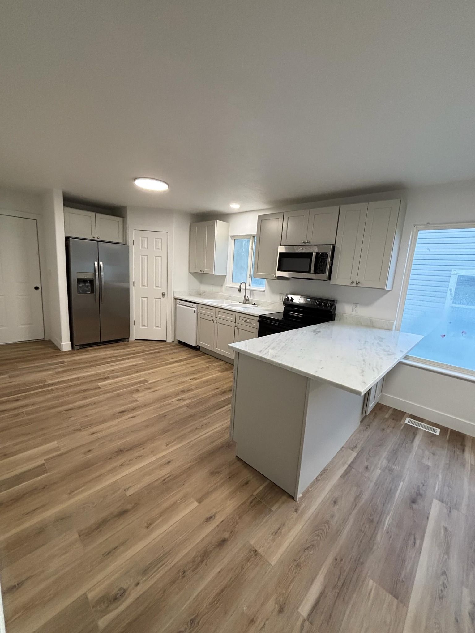 Modern kitchen with white cabinets, stainless steel appliances, and wood flooring.