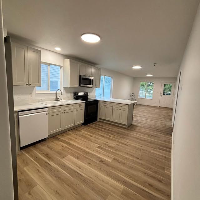 Kitchen with light gray cabinets, white countertops, black appliances, and wood-look flooring.