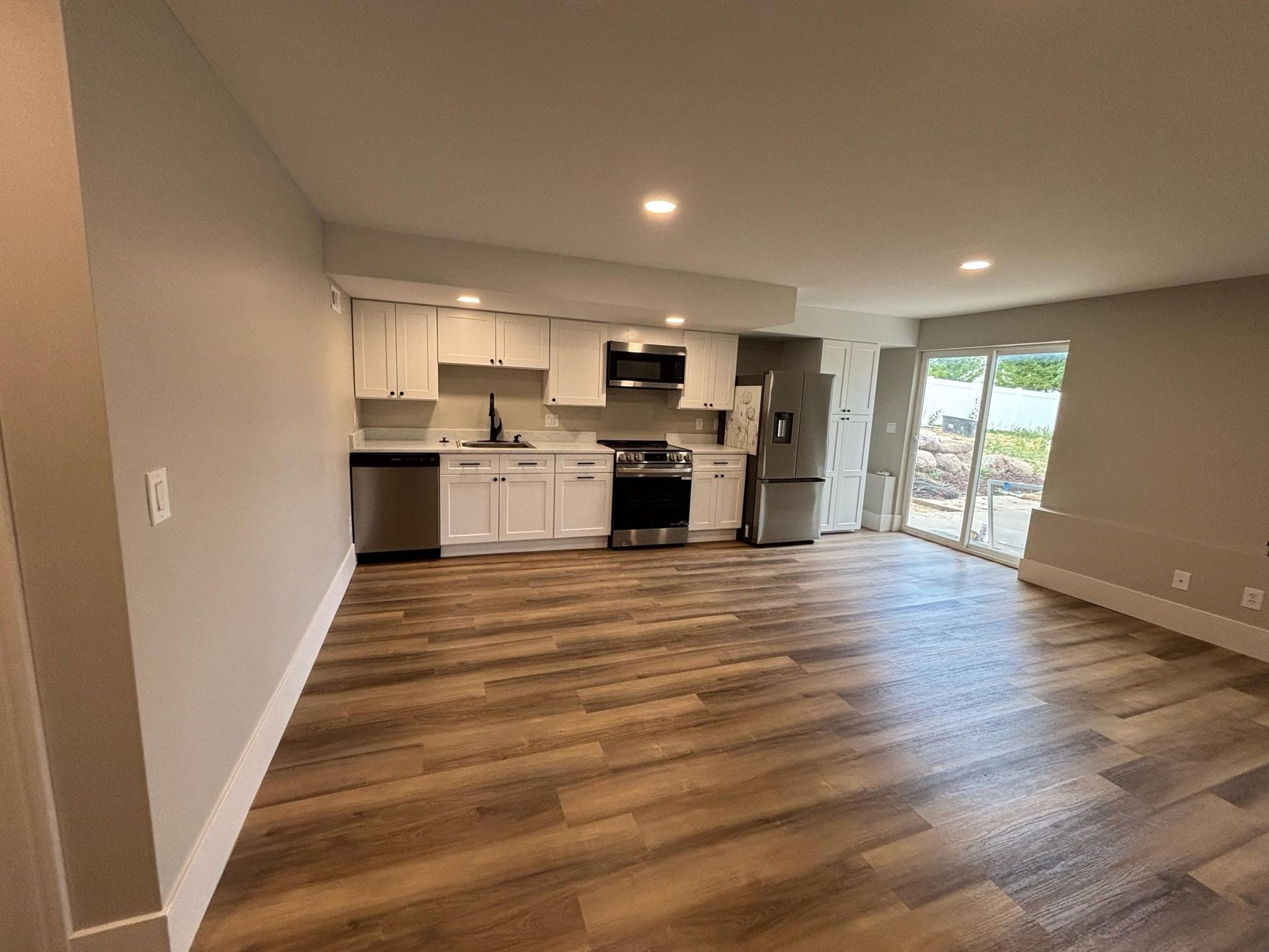 A renovated kitchen with white cabinets, stainless steel appliances, and wood-look flooring.