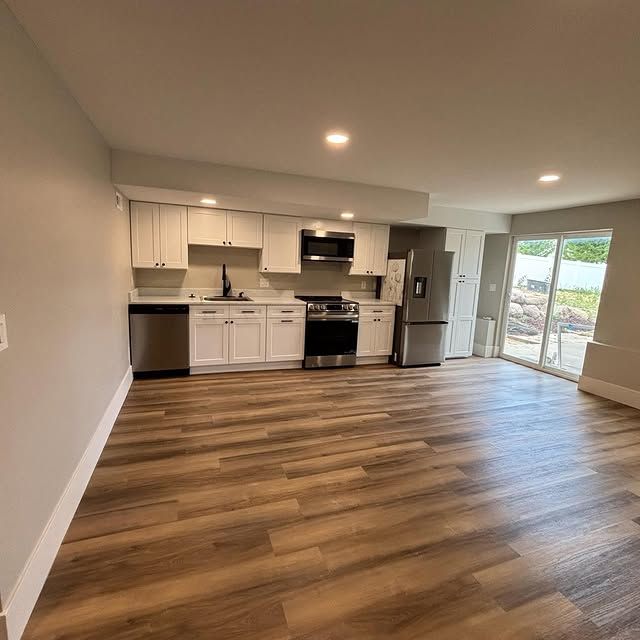 Open-concept kitchen with white cabinets, stainless steel appliances, and wood-look flooring.