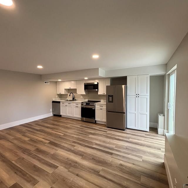 Modern kitchen with white cabinets, stainless steel appliances, and wooden floors.