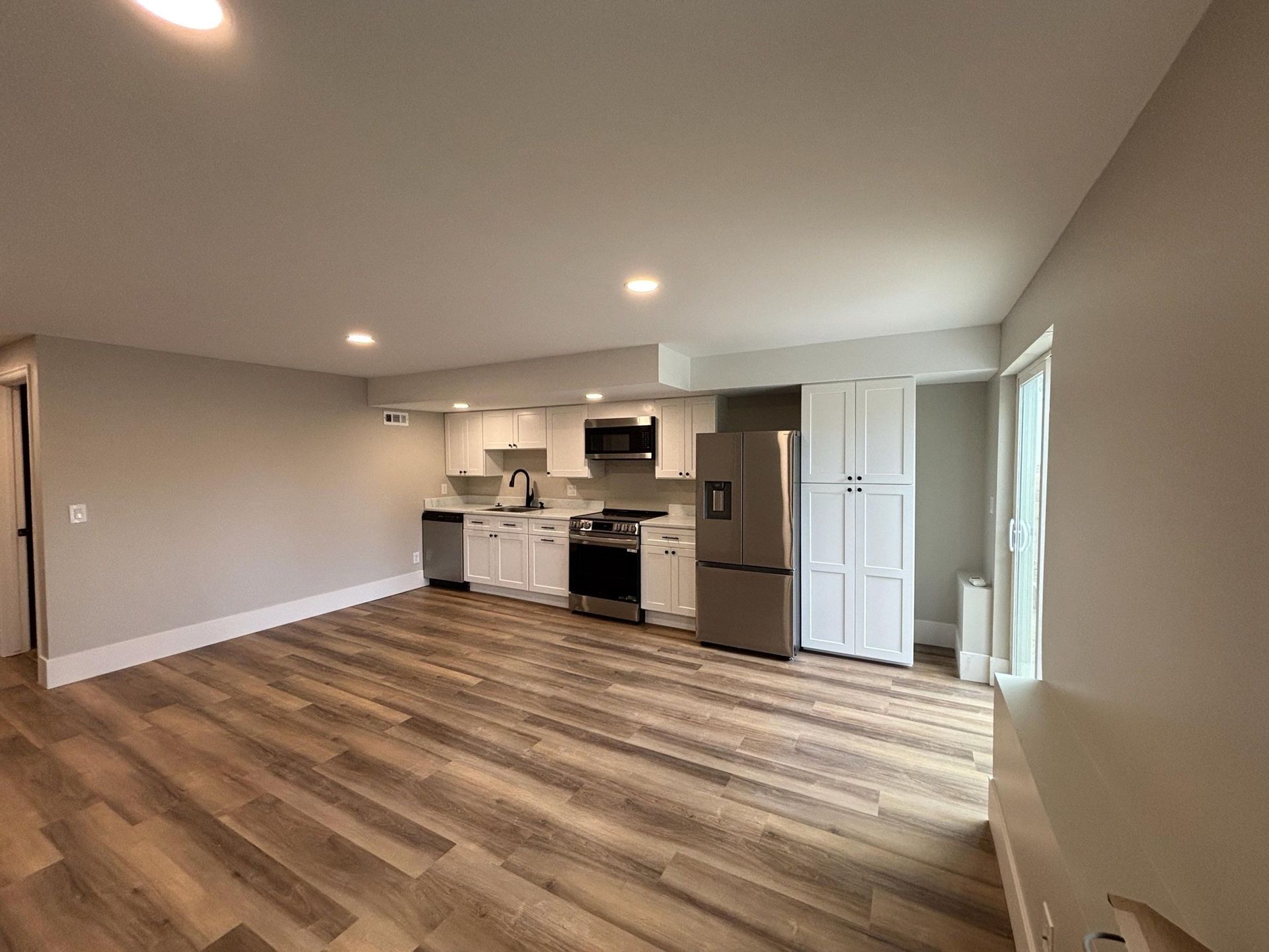 Spacious kitchen with wood floors, white cabinets, stainless steel appliances, and large windows.