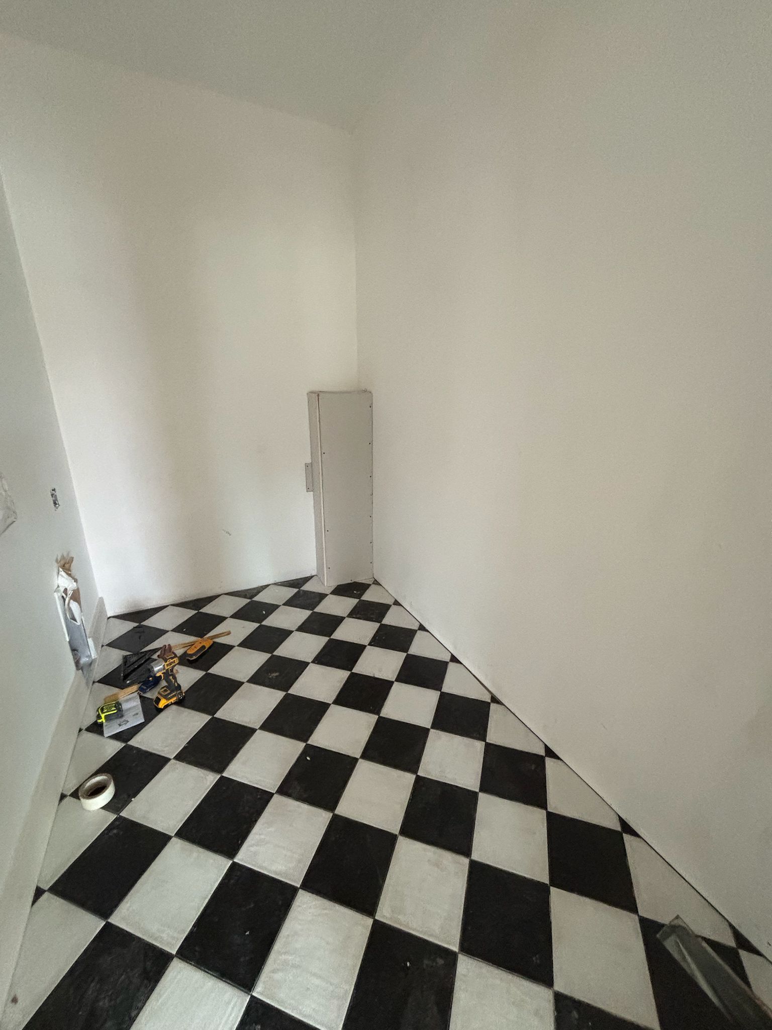 Room with black and white checkered floor, white walls, and a tall, narrow, light-colored cabinet.