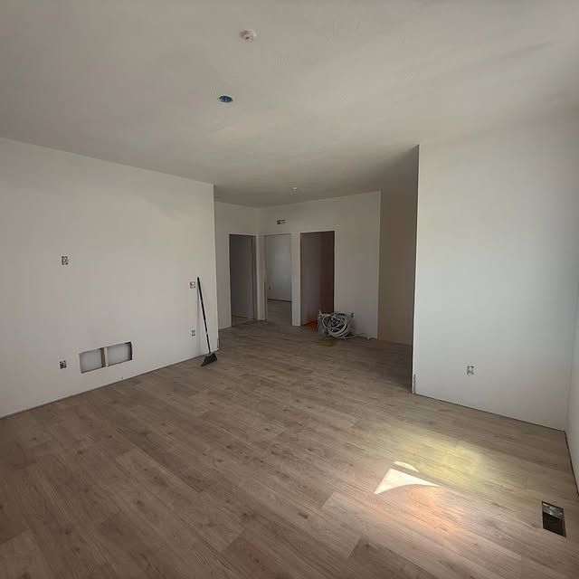 Empty room with light wood flooring and white walls, under construction.