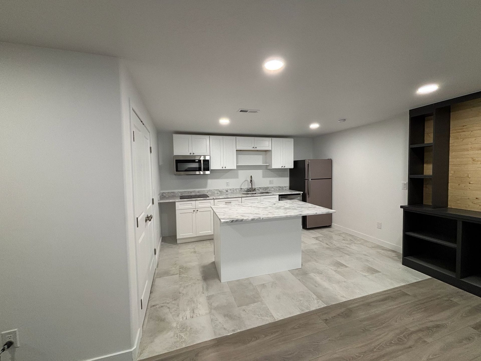Modern kitchen with white cabinets, island, and appliances in a room with light wood-look flooring.