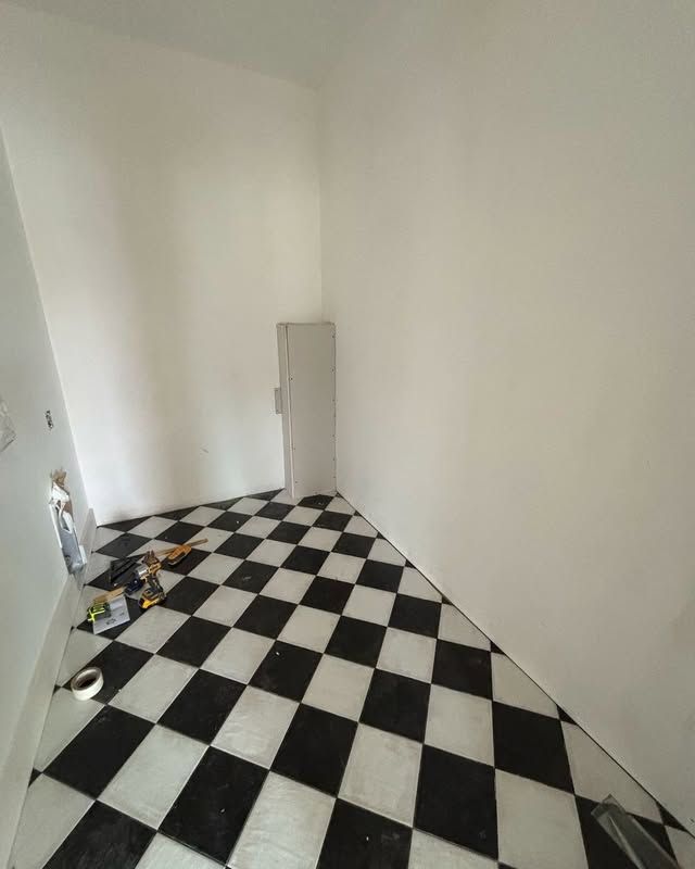 Black and white checkered floor in a room with white walls, a tall cabinet, and some tools.