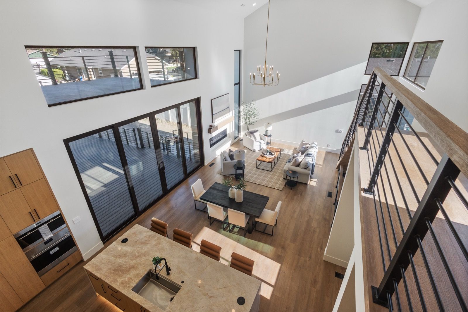 High-angle view of modern home interior: kitchen island, dining table, living room, and balcony with high ceilings.