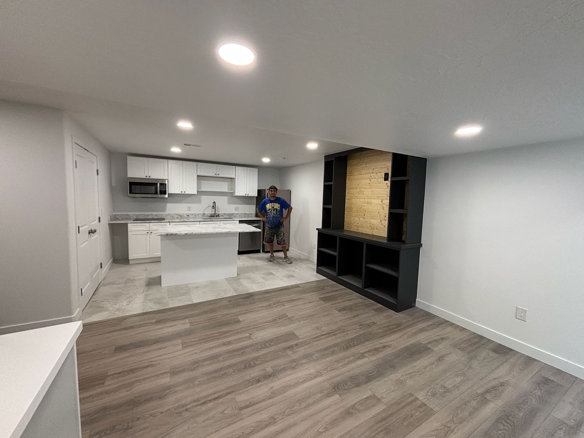 Newly renovated basement apartment with a kitchen, entertainment unit, and a person standing in the center.