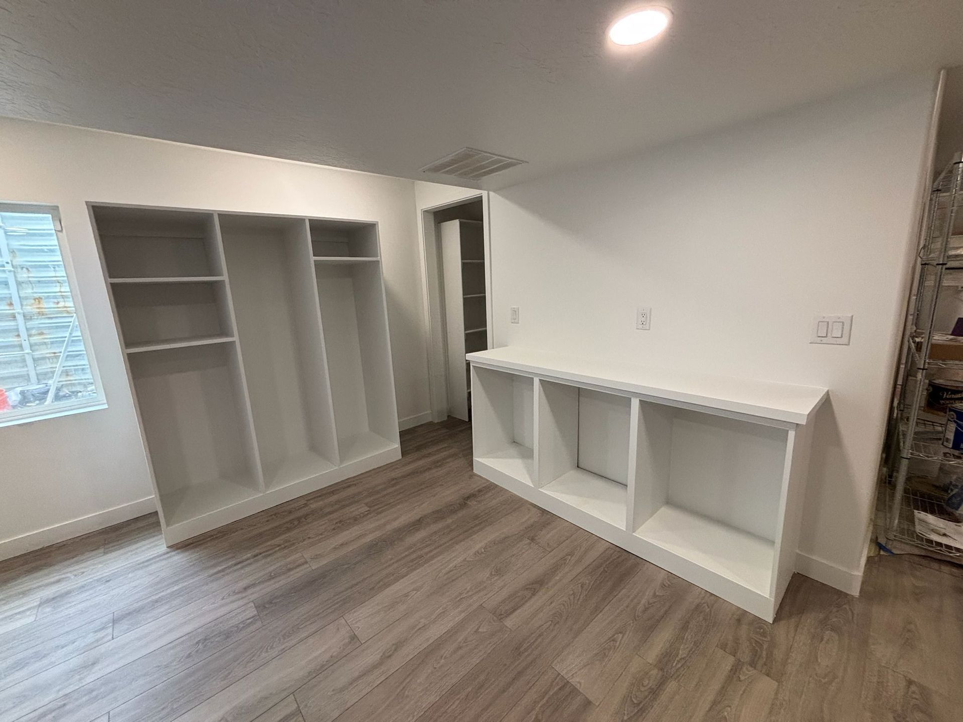Empty white built-in shelves and cabinets in a room with light wood-look flooring and white walls.