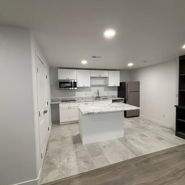 Modern white kitchen with island, white cabinets, and stainless steel appliances.