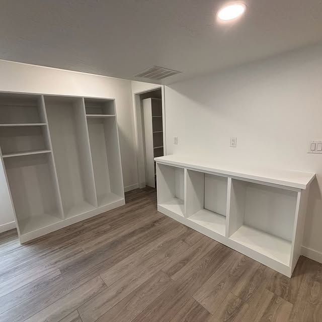 Empty white built-in shelves and cabinets in a room with light wood flooring.