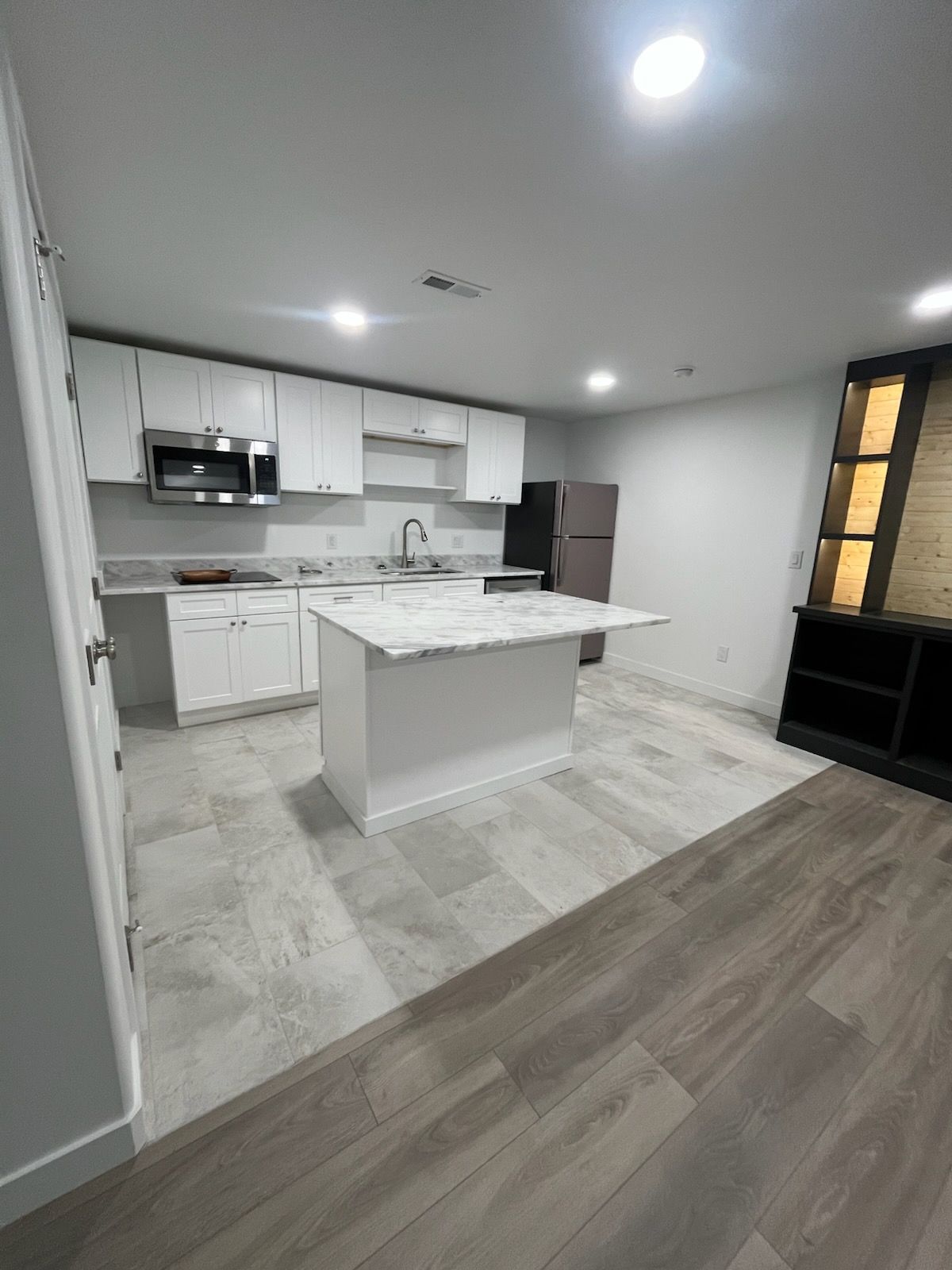 White kitchen with island and stainless steel appliances, grey countertop, and wood-look flooring.