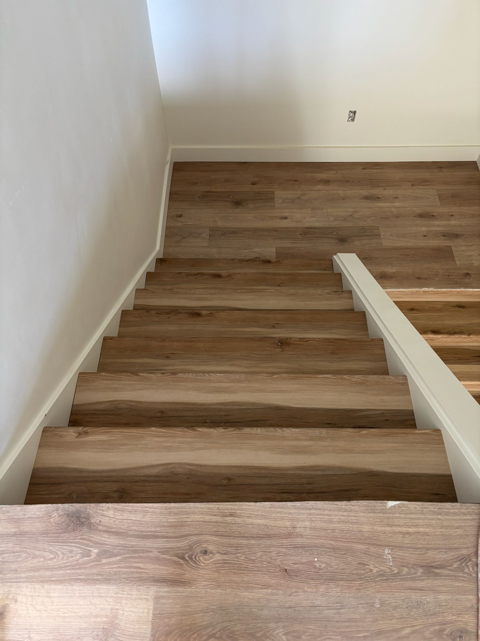 Wooden staircase with light brown flooring and white trim.