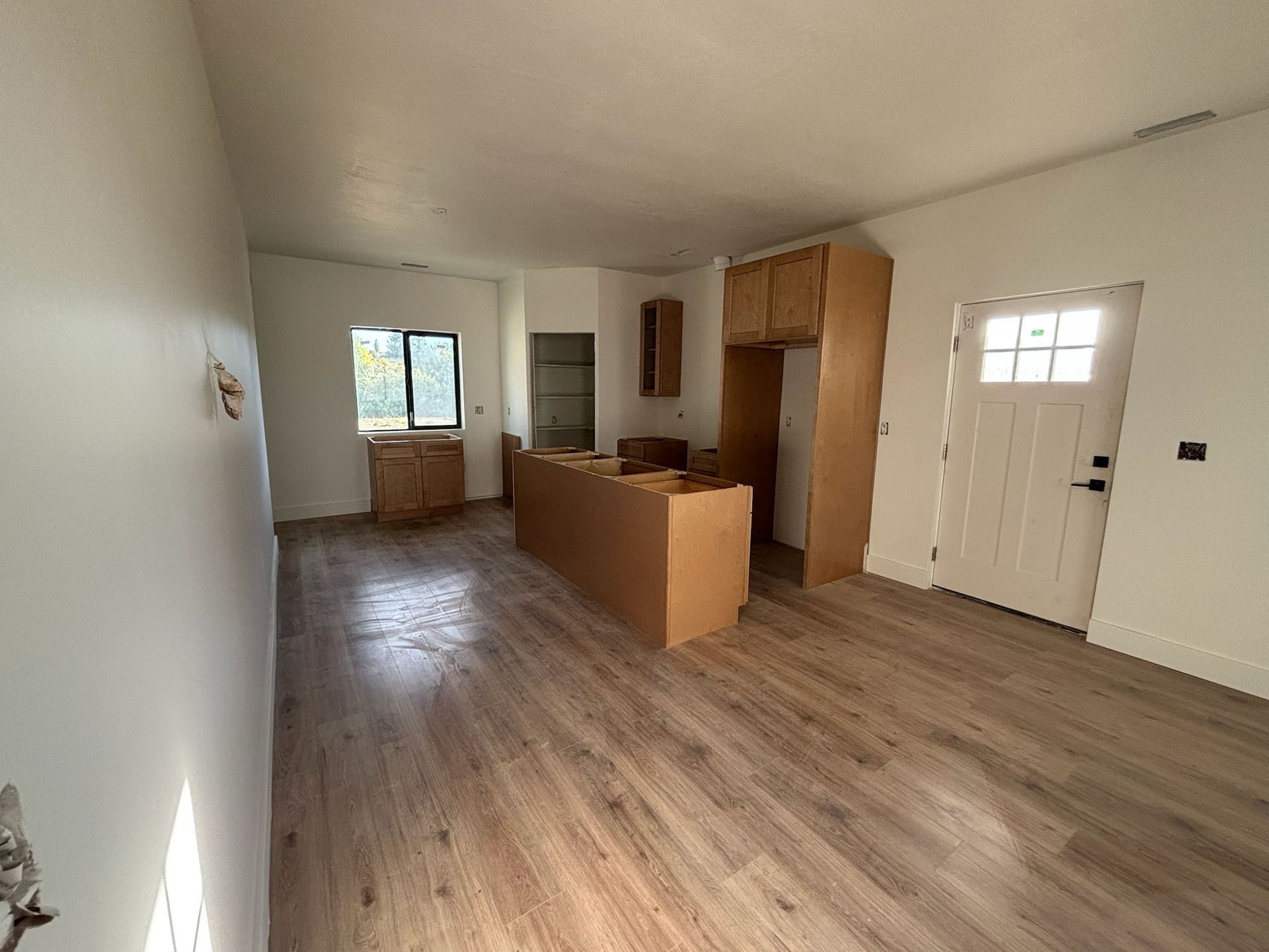 Empty room with new flooring and unfinished kitchen cabinetry. White walls, wood-look floor, cardboard boxes visible.