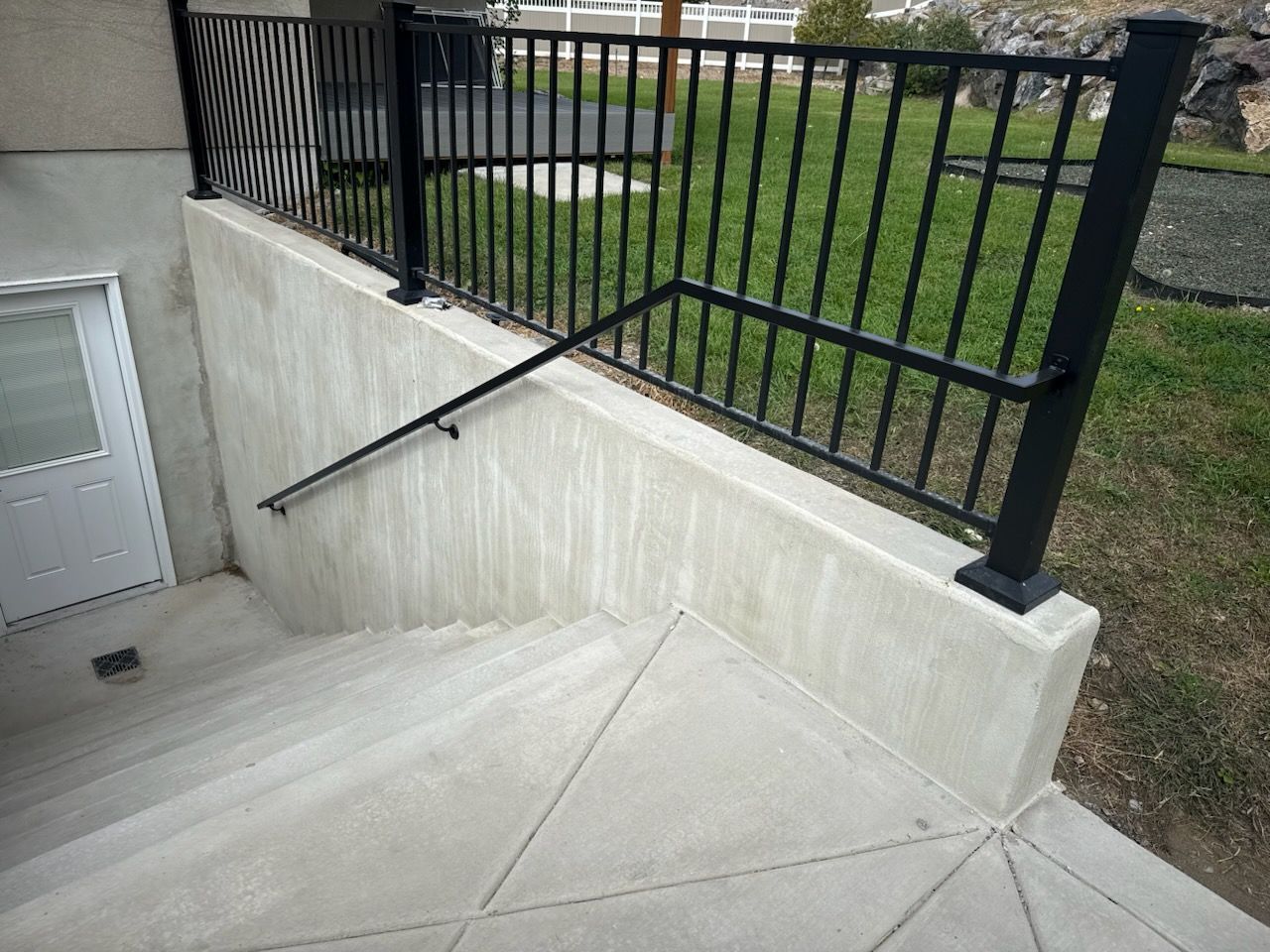 Concrete stairs leading down with black metal railing and a white door to the left.