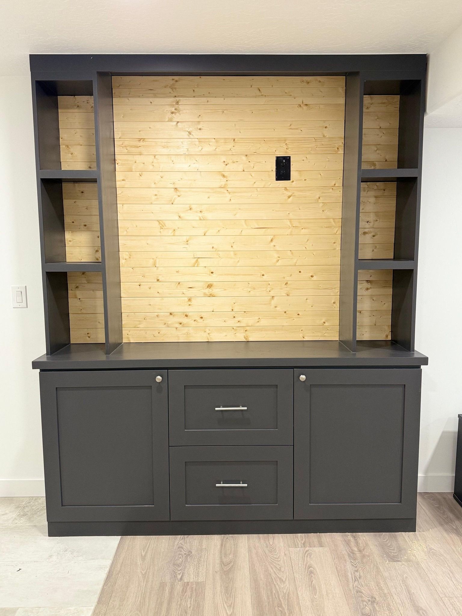Dark gray built-in cabinet with two doors, two drawers, and open shelves; light wood background.