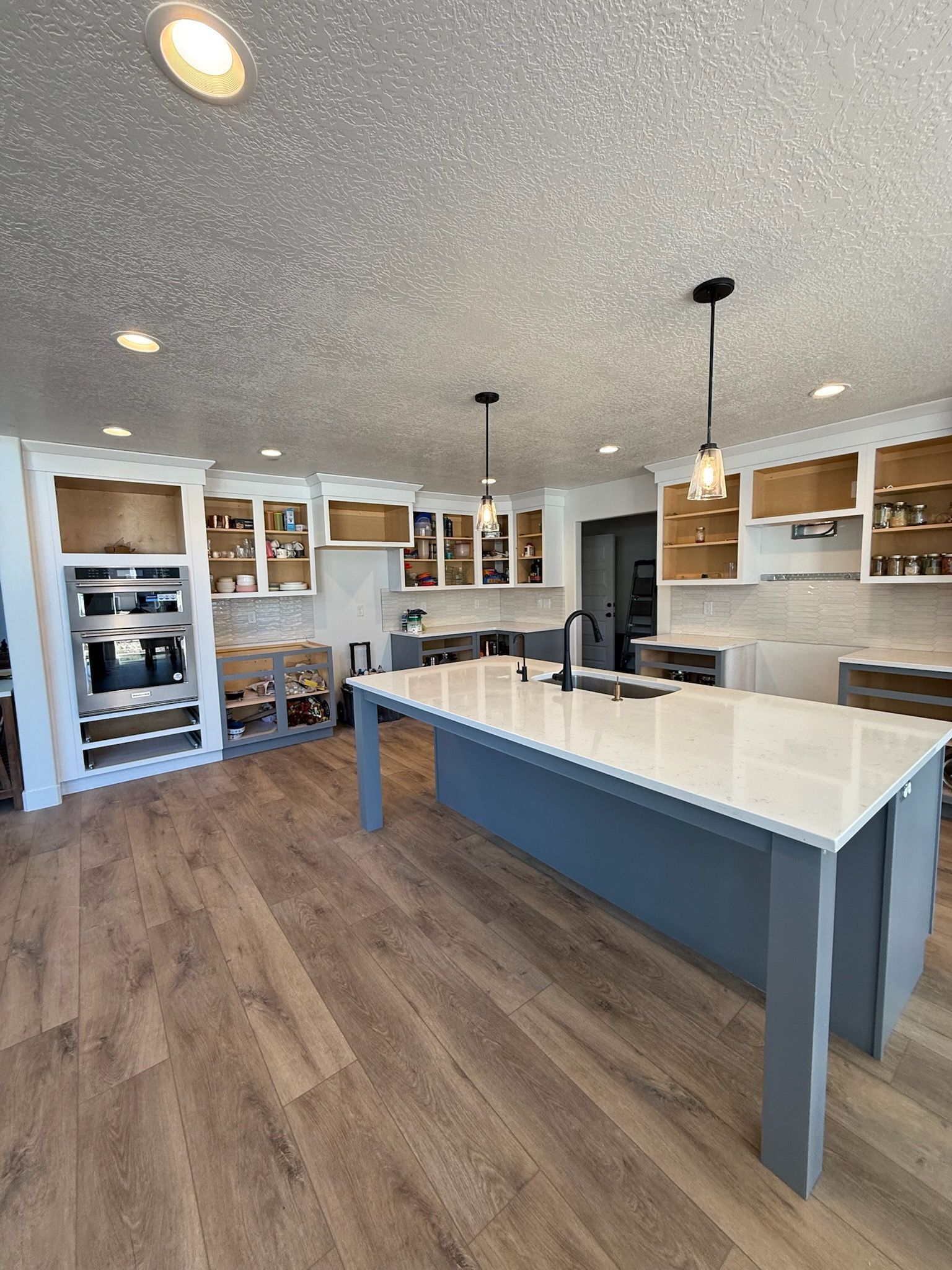 Kitchen with white cabinets, gray island, and wood-look flooring. Partially completed remodel.