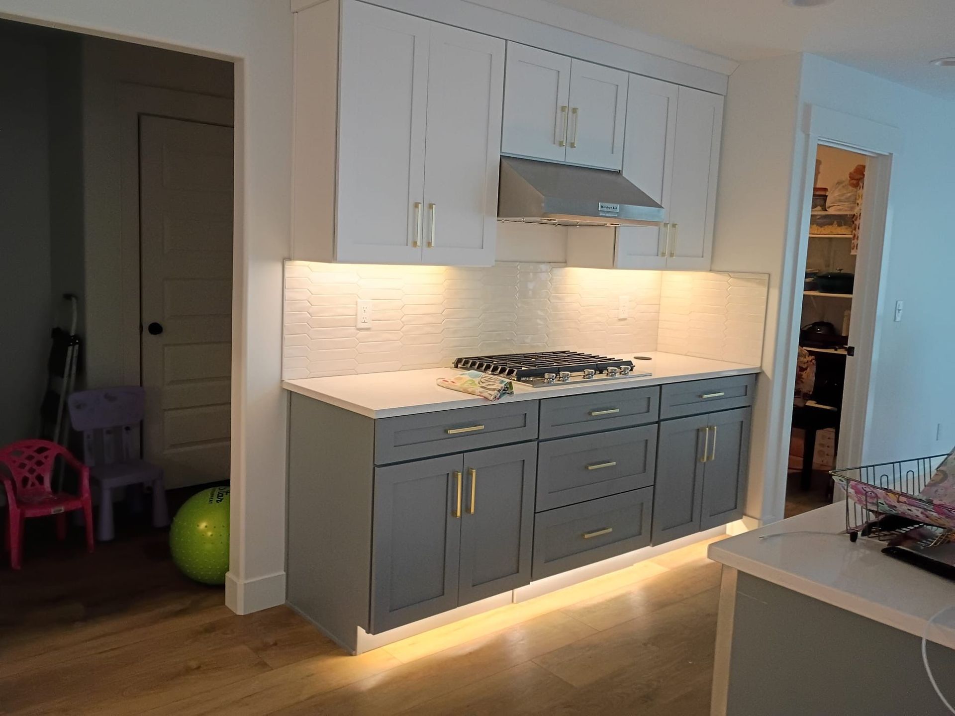 Kitchen cabinets with a gray lower and white upper section. Backsplash and under-cabinet lighting.