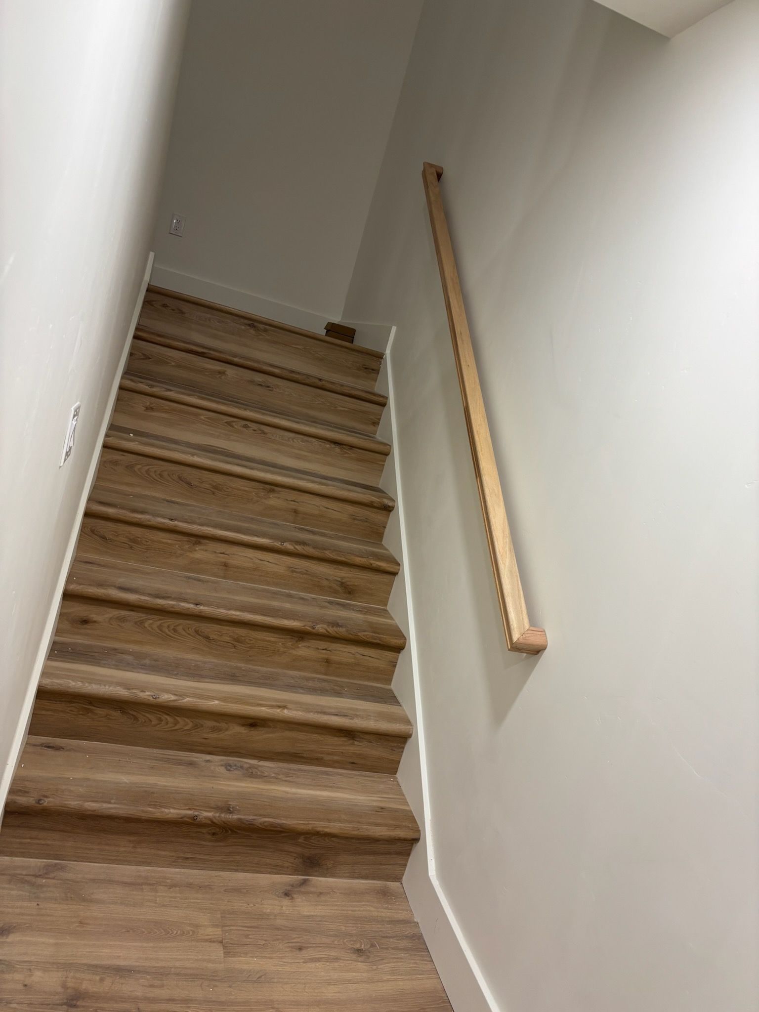 Wooden staircase with a handrail against a light gray wall.