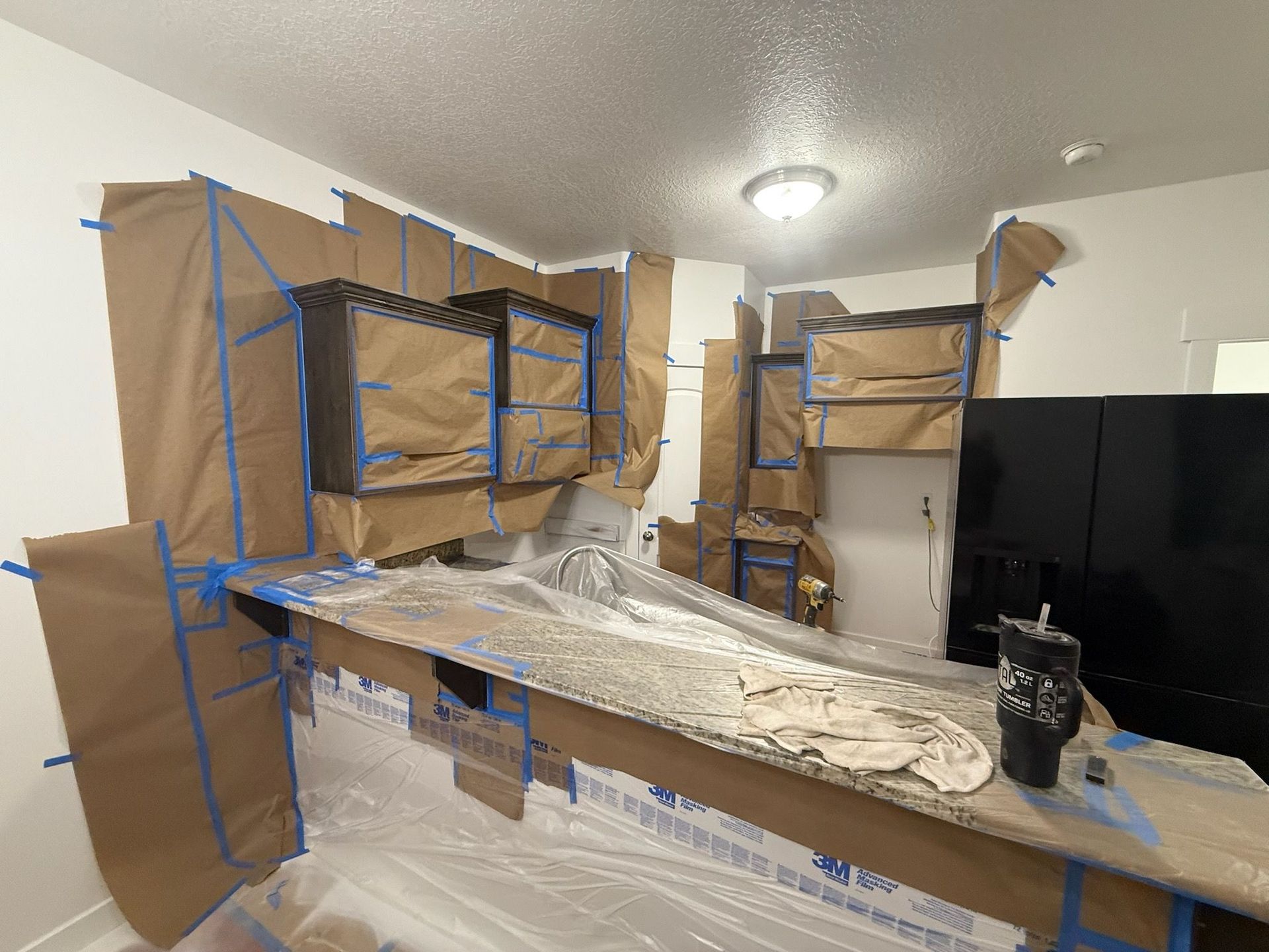 Room with furniture covered in paper and tape, prepared for painting.