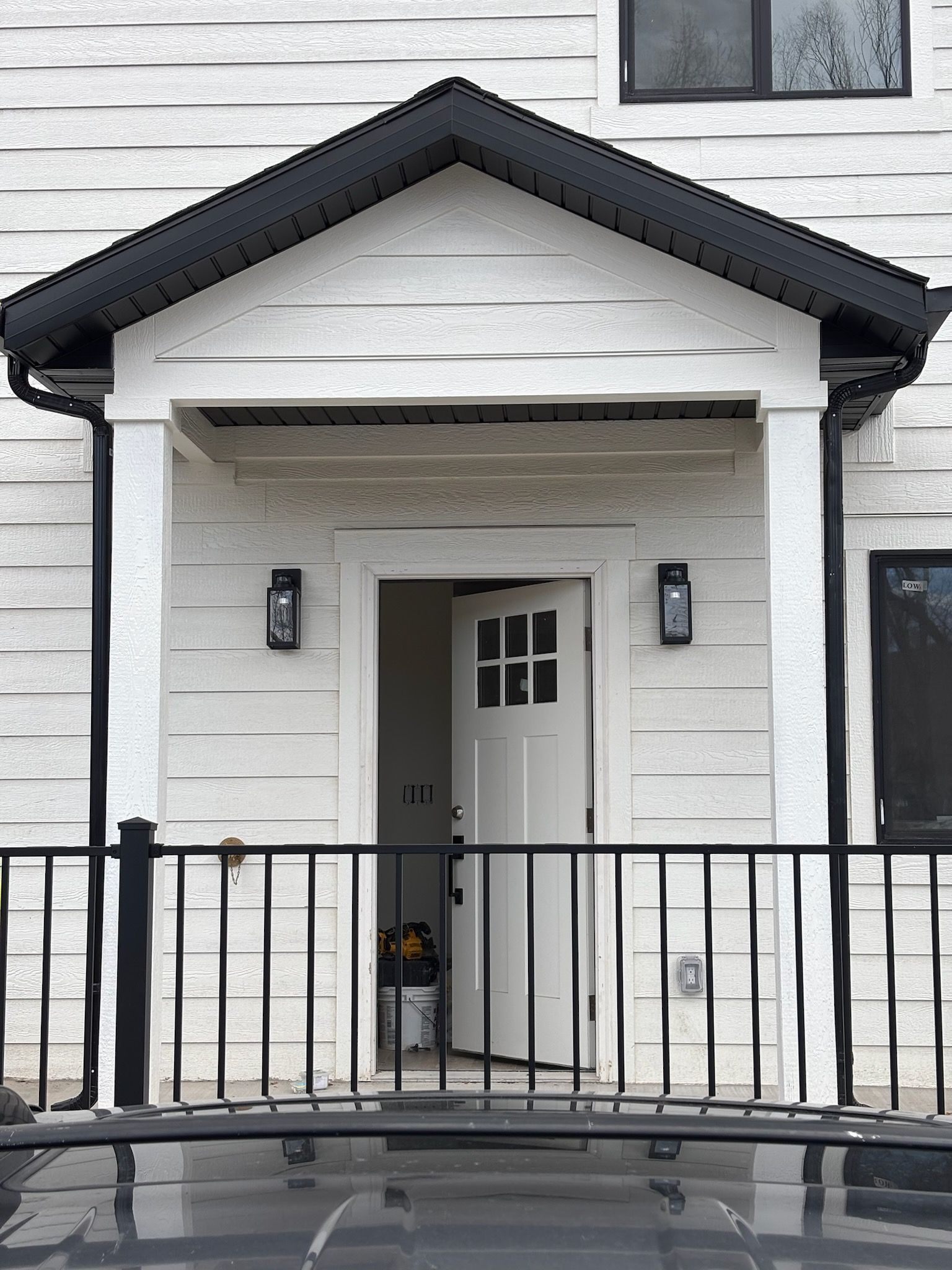 White entrance with open door, black railing, sconces on either side.
