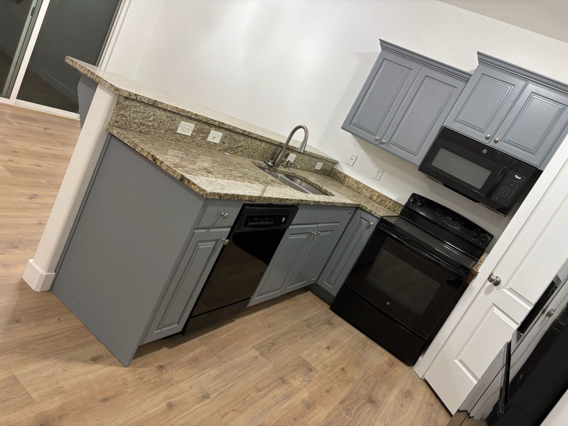 Gray kitchen cabinets with granite countertops, black appliances, and light wood flooring.