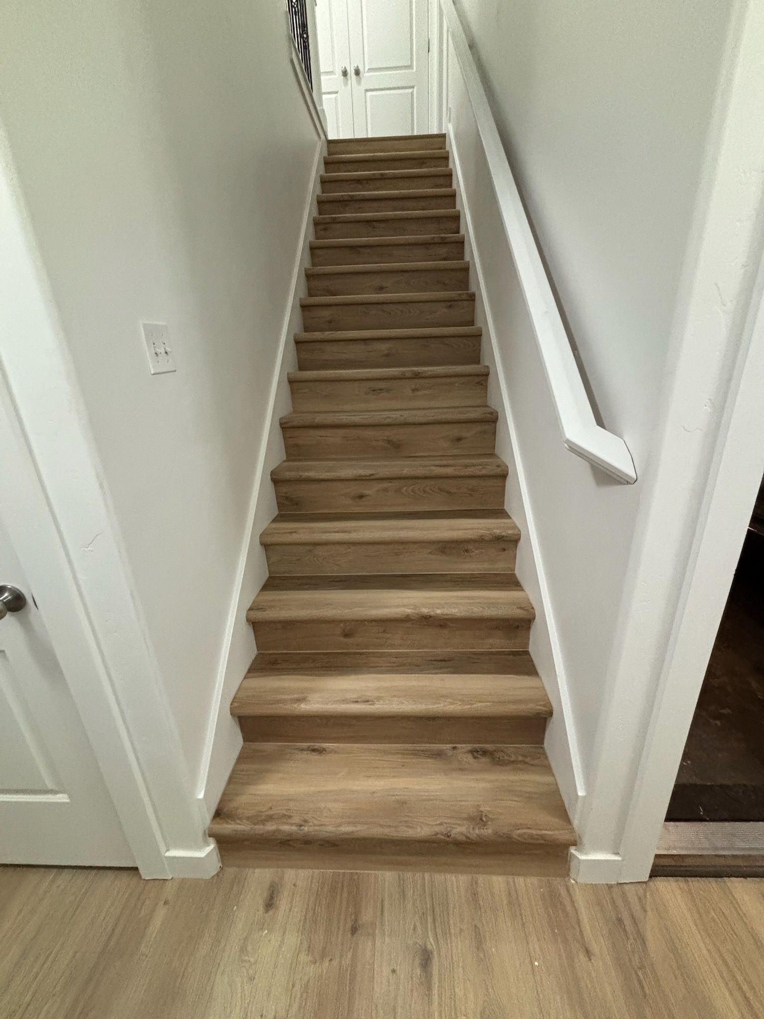 Staircase with wooden steps and white walls; a handrail on the right side.