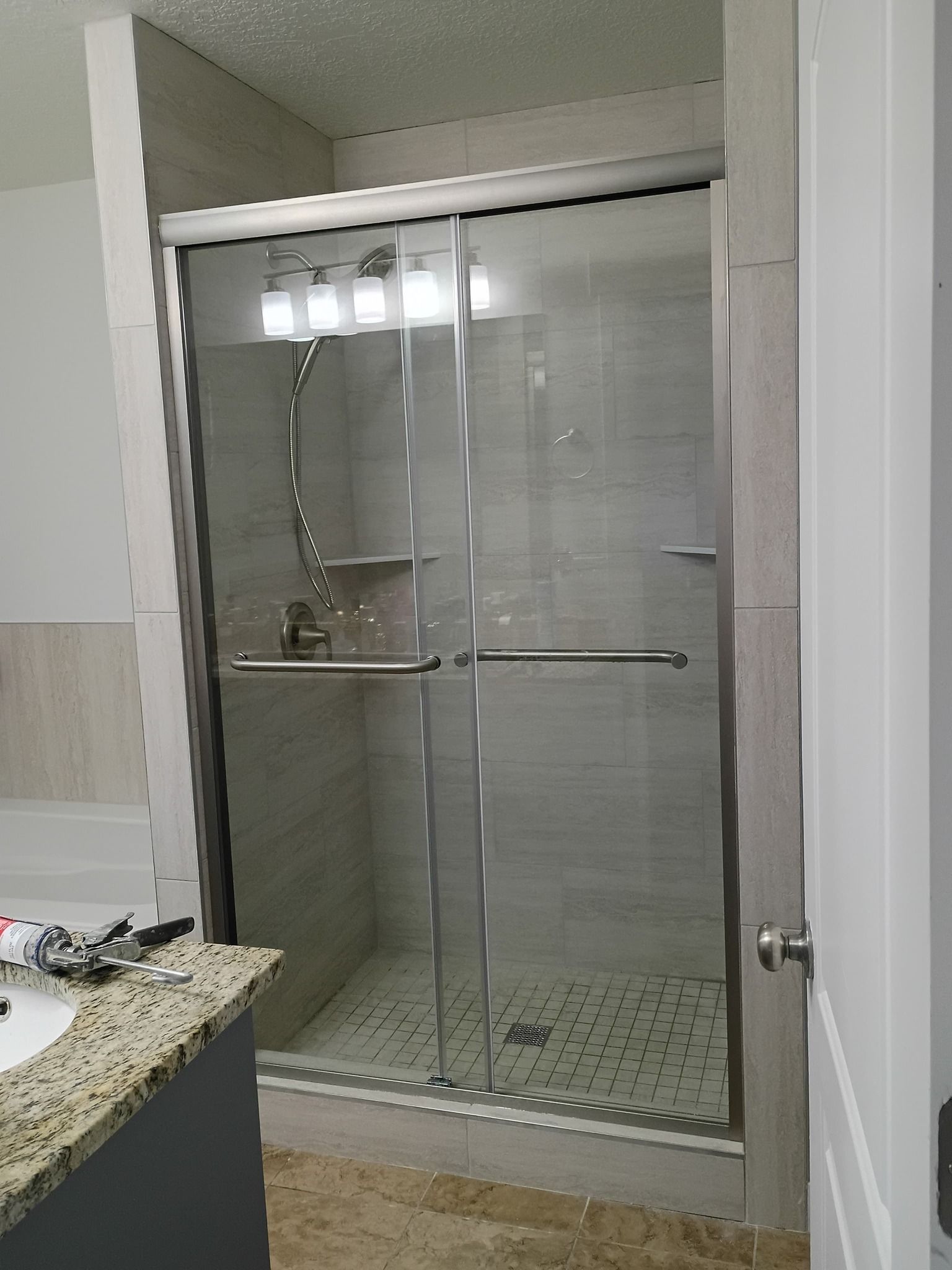 Glass-door shower with gray tile walls, and a granite countertop vanity.