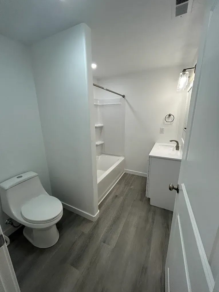 White bathroom with toilet, sink, and shower/tub. Gray flooring.