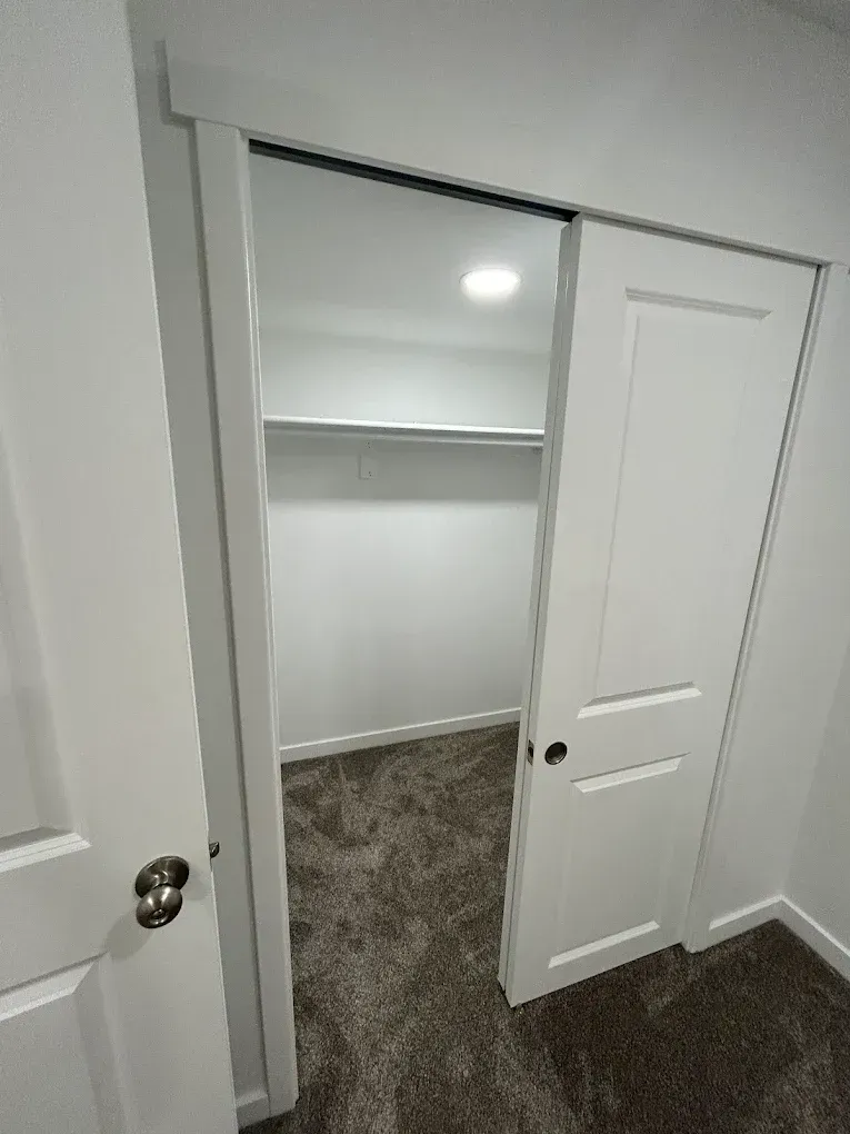 White closet with sliding door open, revealing a carpeted interior, a clothes rod, and a light.