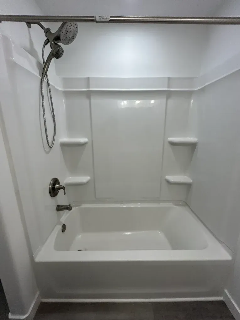 White bathtub and shower combo with built-in shelves. Silver showerhead and faucet.