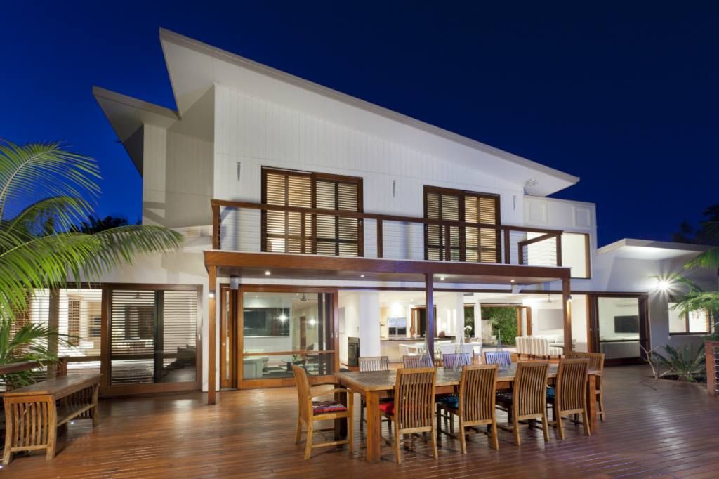 A modern two-story home with a wooden balcony and deck at dusk, featuring a dining set on the patio.