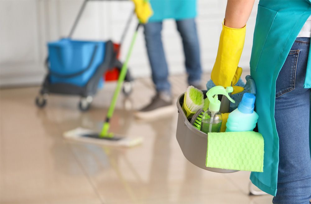 A woman is holding a bucket of cleaning supplies in a room.