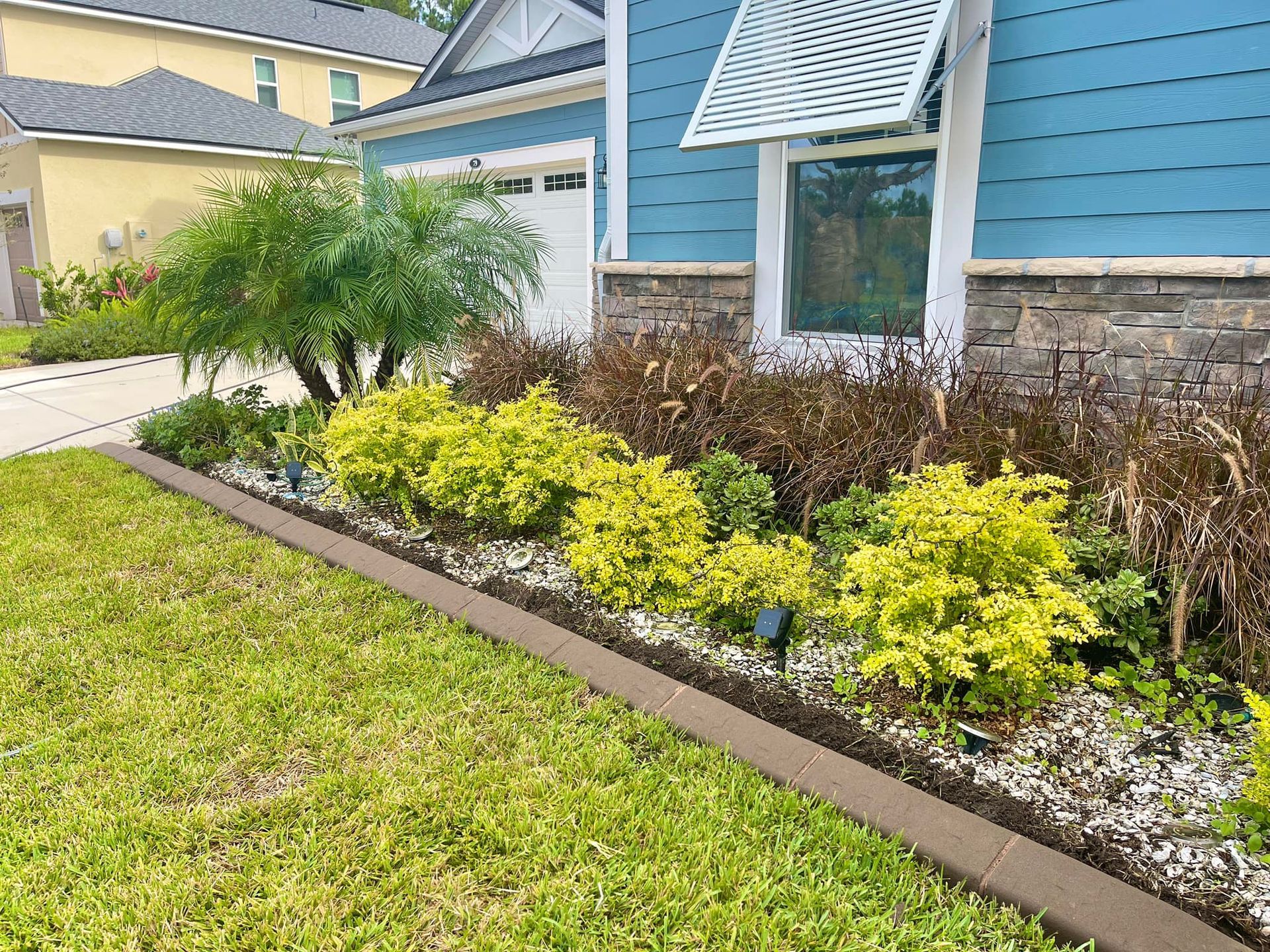 A house with a blue siding and a garden in front of it.