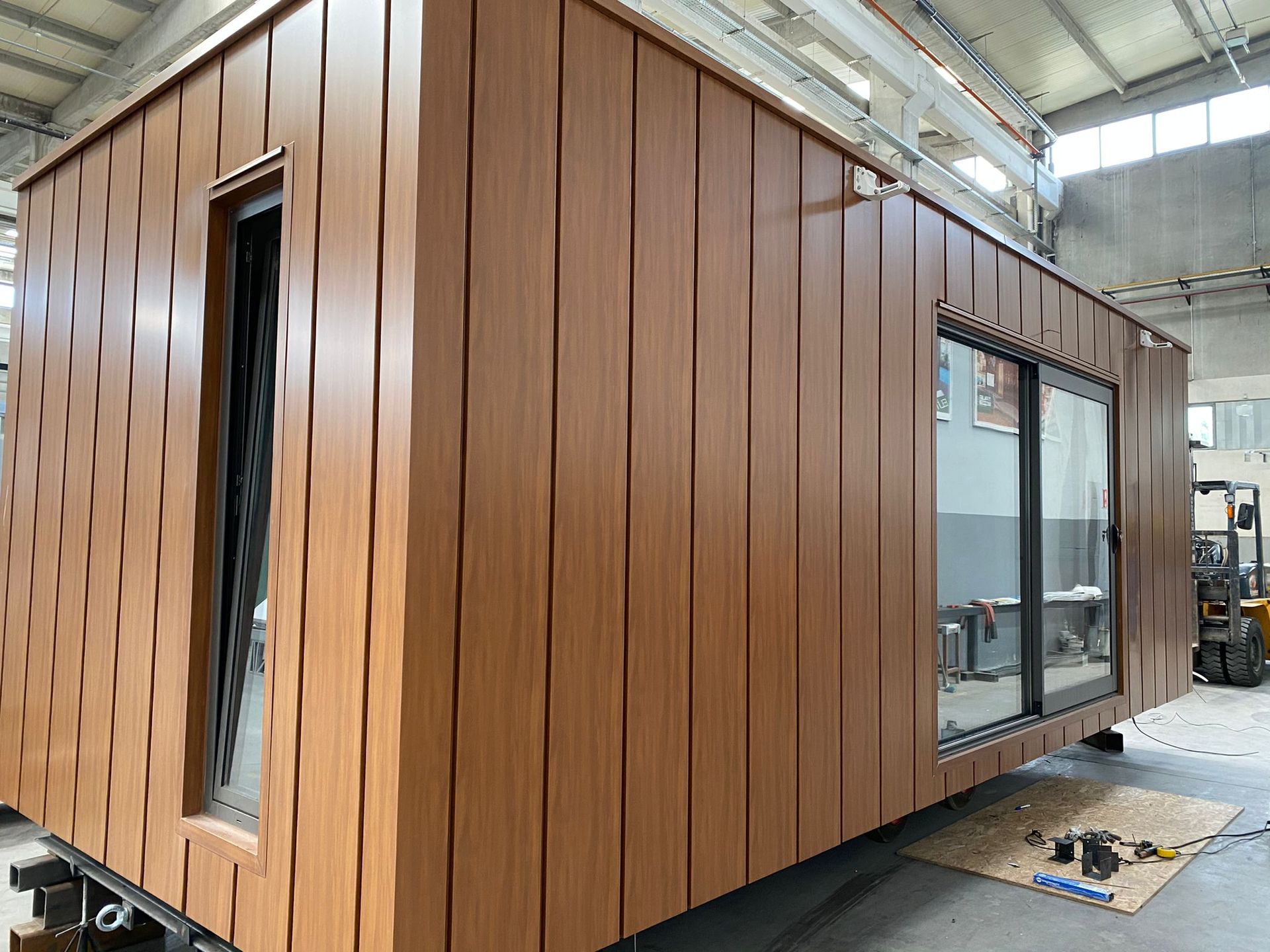 In een fabriek wordt een houten huis met veel ramen gebouwd.