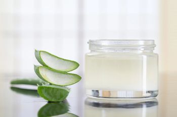Hojas de aloe vera y un tarro de yogur sobre una mesa.