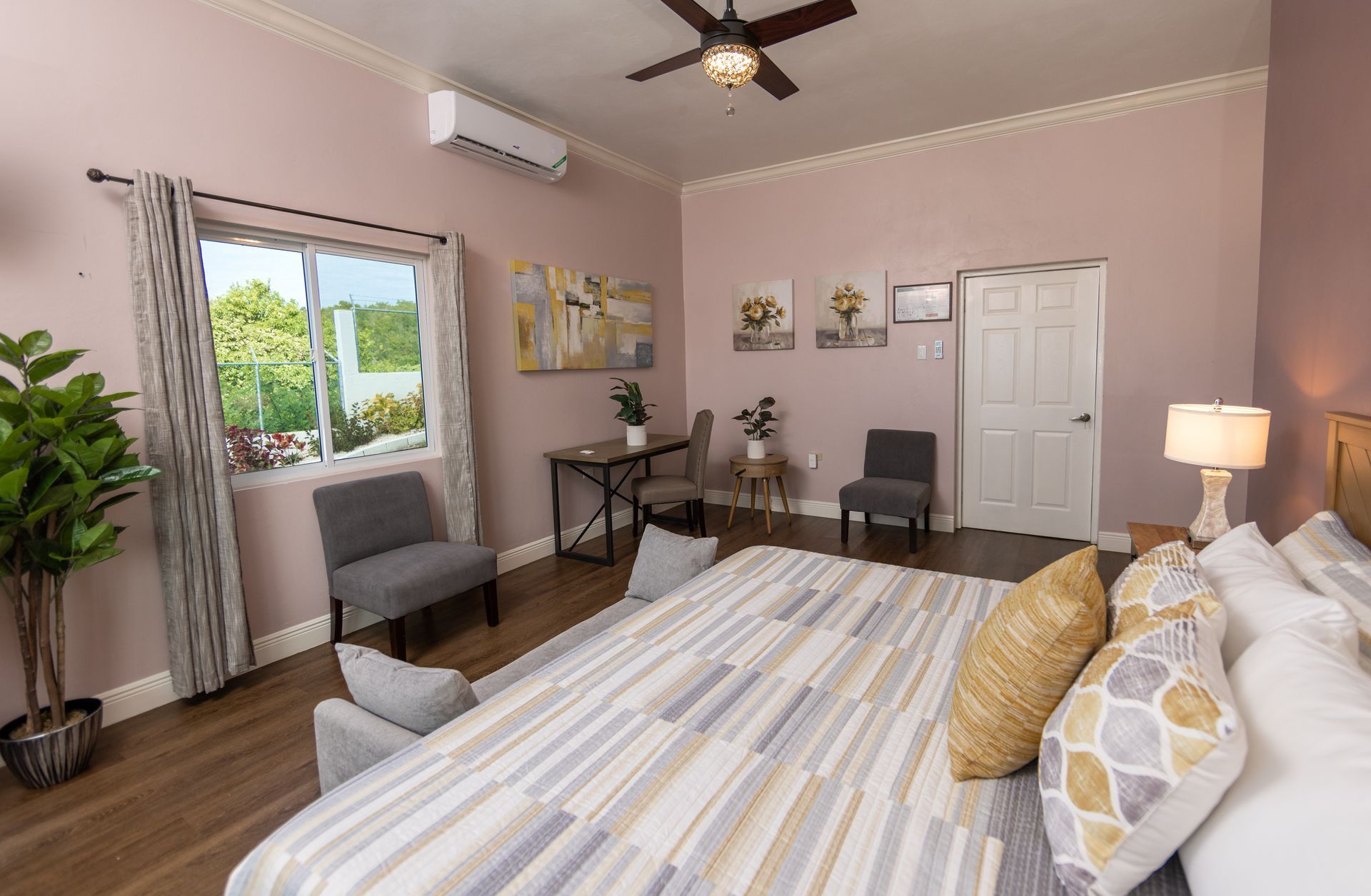 Bedroom with a large bed, chairs, a desk, a window with greenery view, and decorative artwork on the wall.