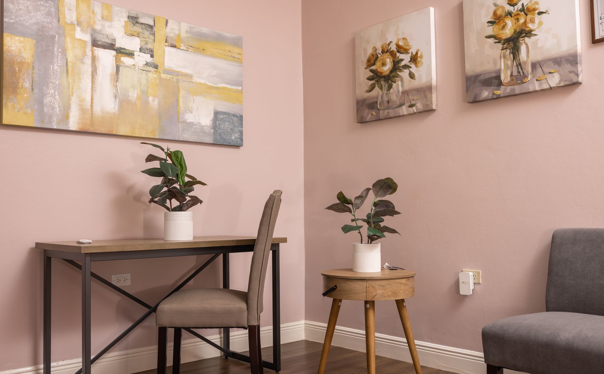 Corner office with desk, chair, plants, artwork on pink walls.